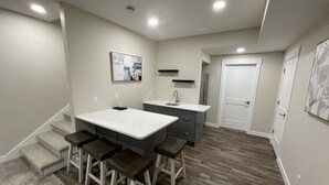A modern kitchen with a central island, bar stools, a built-in sink, and a staircase leading to another level. - New Construction Home, 1 block to Legendary Surf District/ Blocks to downtown (Clear Lake)