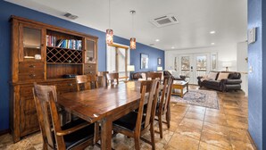 A dining area with a wooden table and chairs, a built-in bookshelf, and a view of the living room through a glass door. - Home on the Range Near Glacier Park (Columbia Falls)