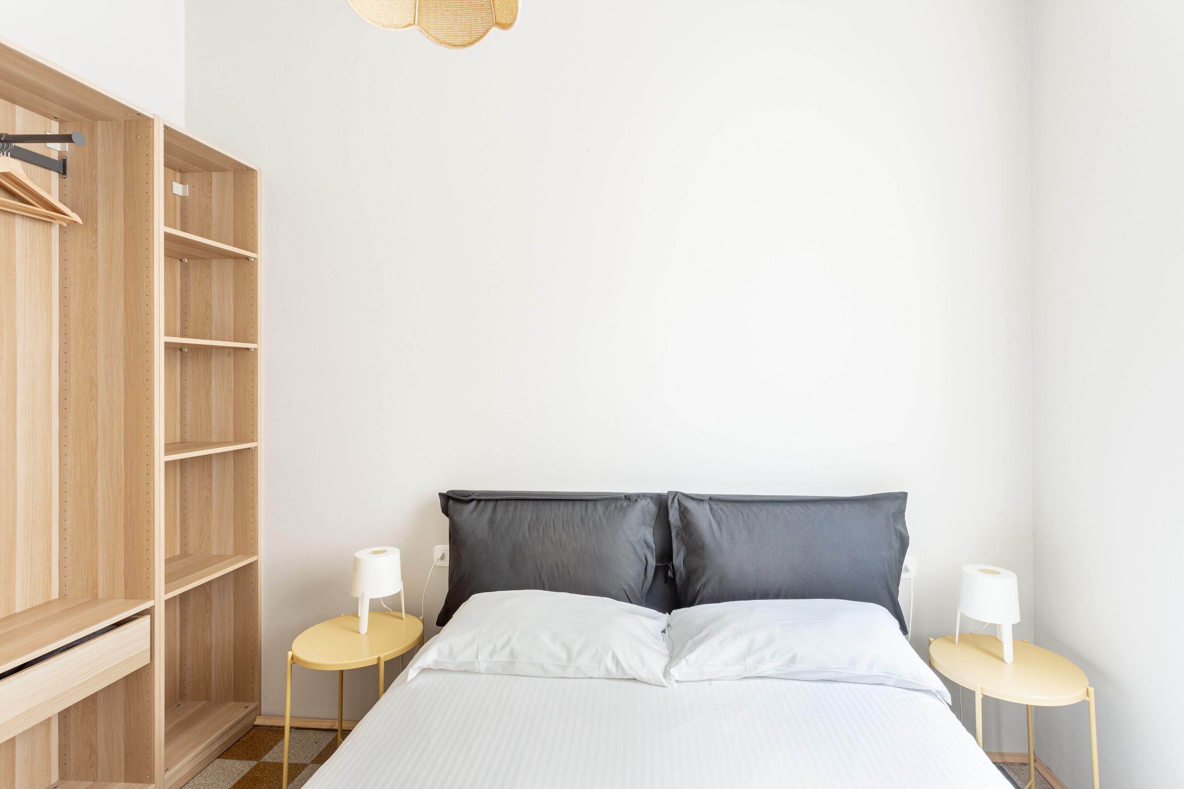 A bedroom with a bed, two bedside tables, a wardrobe, and a hanging light fixture.