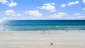 Una amplia playa de arena con cielo azul despejado y mar tranquilo.