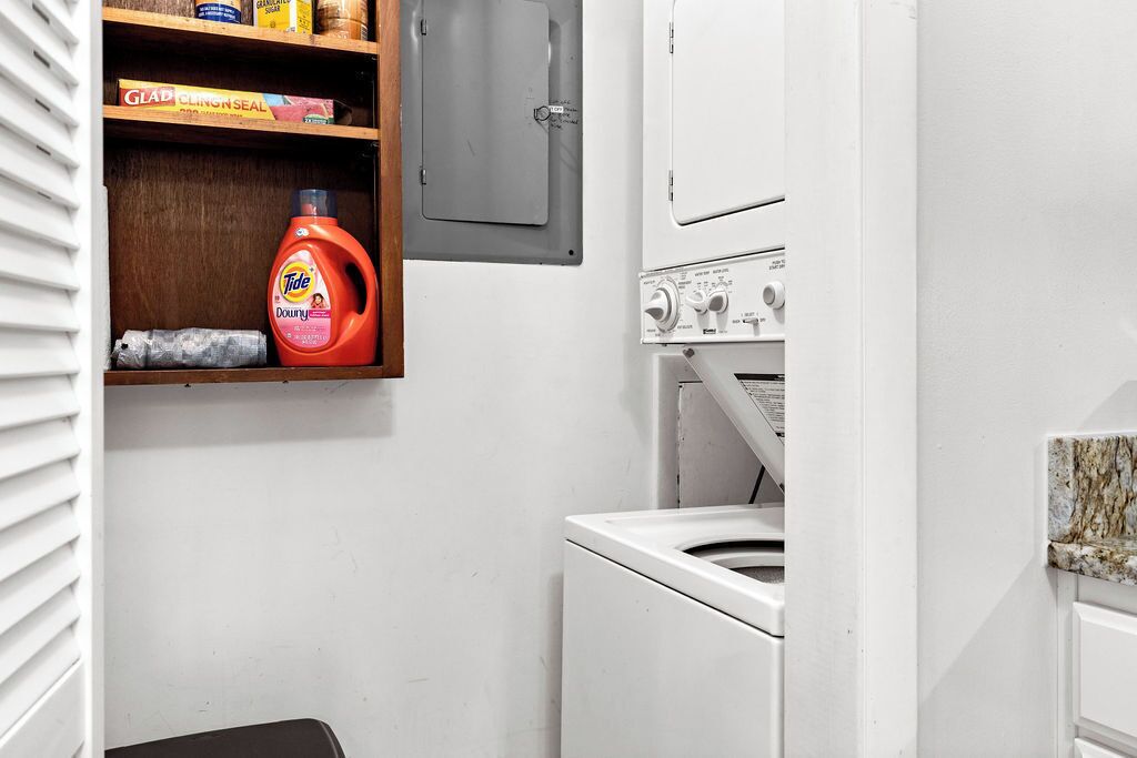 Un espace buanderie comprenant un lave-linge, une étagère avec des produits de nettoyage et un placard.