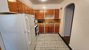 Cocina compacta con armarios de madera, un refrigerador blanco, microondas y pileta.