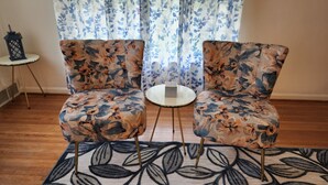 Una habitación con dos sillones de brazos con estampado floral, una mesita redonda y un tapete con diseño en el suelo.