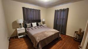 Un dormitorio con cama, dos mesitas de noche con lámparas, cabecero y una pequeña mesita con un objeto decorativo.