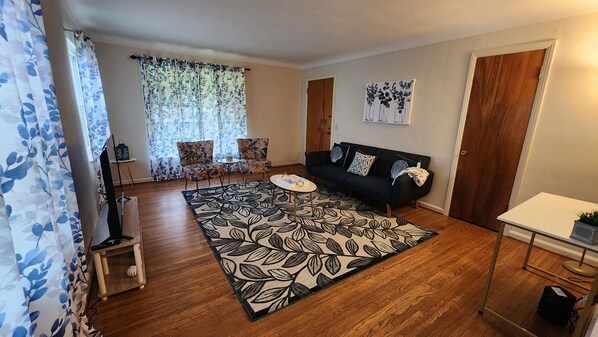 A living room with a dark sofa, floral-patterned chairs, a coffee table, and a patterned rug.