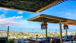 A rooftop terrace with outdoor seating, a pergola, hanging floral decorations, and a cityscape view. - Enjoy a fully equipped private and elegant condo in a luxury building.  (Cabo San Lucas)