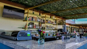 A bar area with a counter, shelves of liquor bottles, a grill, and a TV mounted on the wall. - Enjoy a fully equipped private and elegant condo in a luxury building.  (Cabo San Lucas)