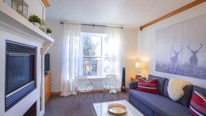 A living room with a fireplace, a sofa, two chairs, a coffee table, and a window with curtains. - Cozy Brian Head Condo: Walk to Navajo Express Lift (Brian Head)