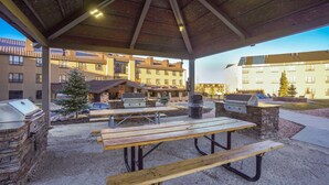 An outdoor patio area with barbecue grills, picnic tables, and a covered shelter. - Cozy Brian Head Condo: Walk to Navajo Express Lift (Brian Head)