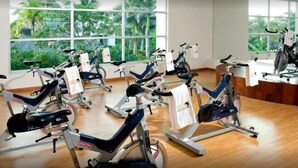 Une salle de sport avec des vélos d’appartement disposés en rangées, de grandes fenêtres donnant sur un espace verdoyant et un plancher en bois.