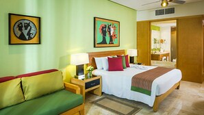 Une chambre d’hôtel avec un lit, un canapé vert, une table de chevet avec une lampe, et deux œuvres d’art encadrées accrochées au mur.