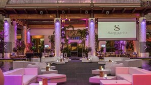 Un hall spacieux doté d’un grand écran diffusant des images de « Santuario », entouré de canapés et de tables blancs, avec une piscine et des plantes tropicales en arrière-plan.
