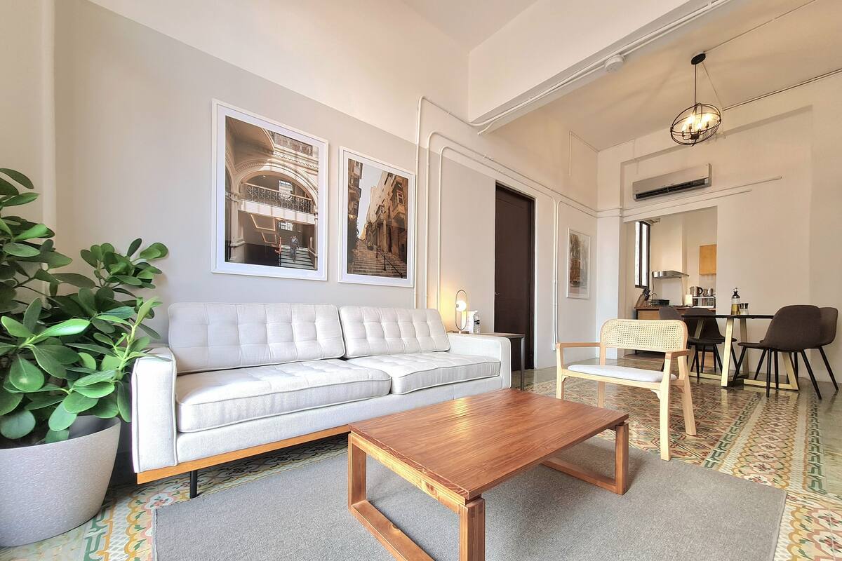 Uma sala de estar moderna com sofá, mesa de centro de madeira e área de jantar com cadeiras e mesa.