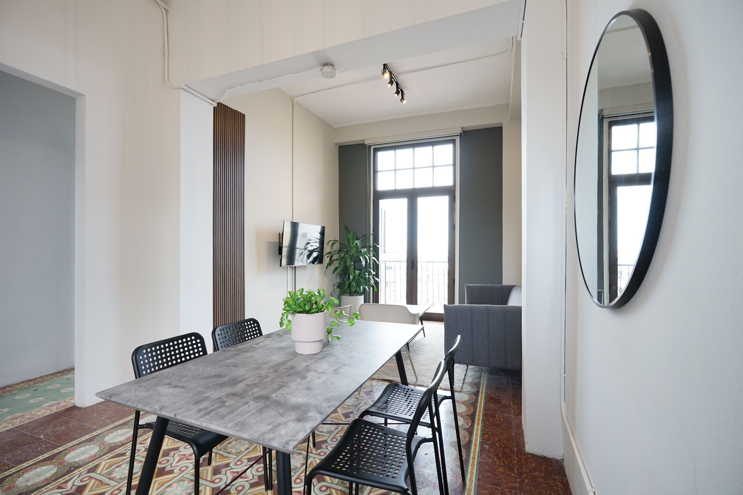 Un comedor moderno con una mesa gris, sillas negras, una planta en maceta y un espejo grande en la pared.