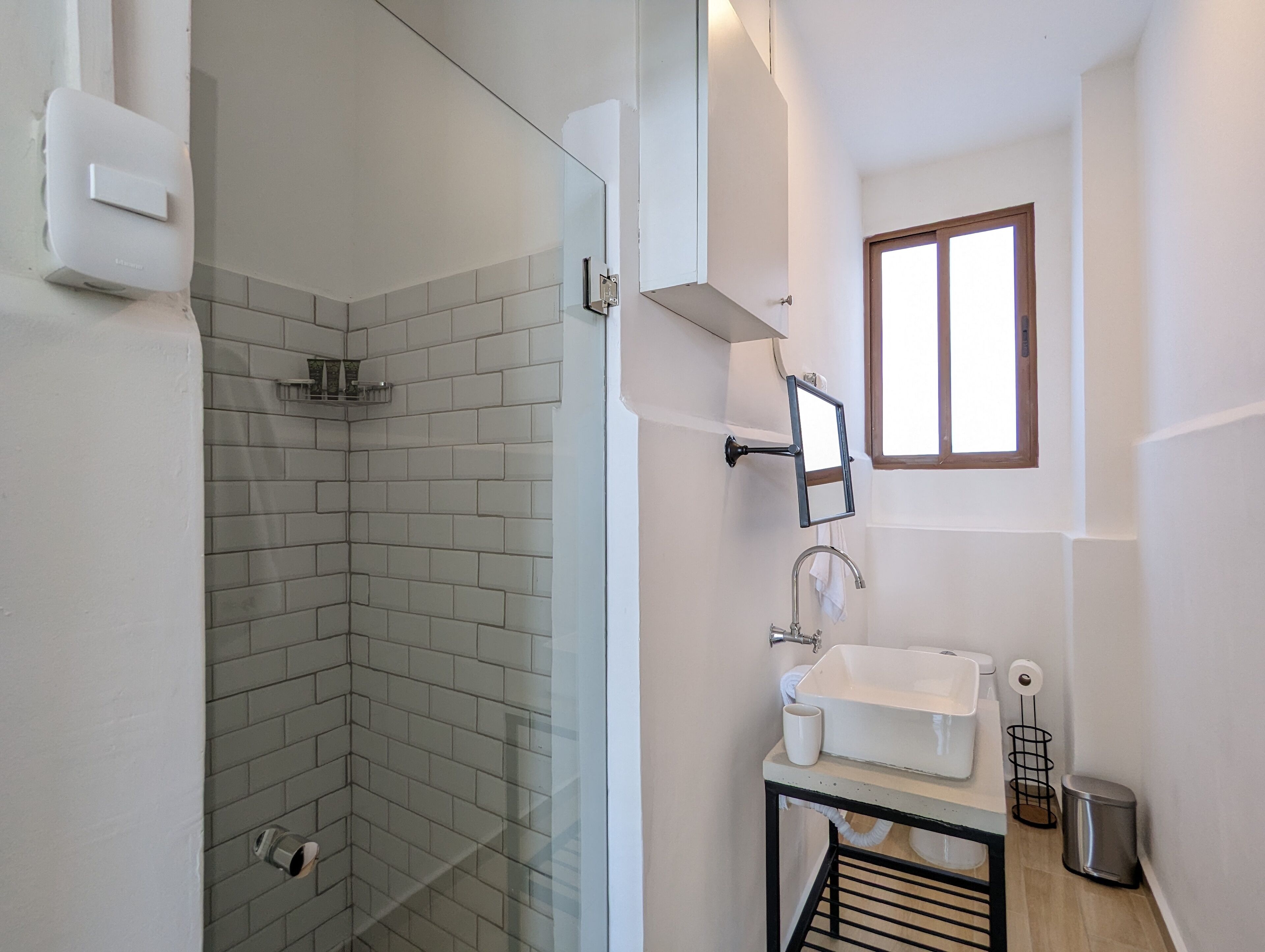 A modern bathroom with a glass shower enclosure, a white sink, and a small window.