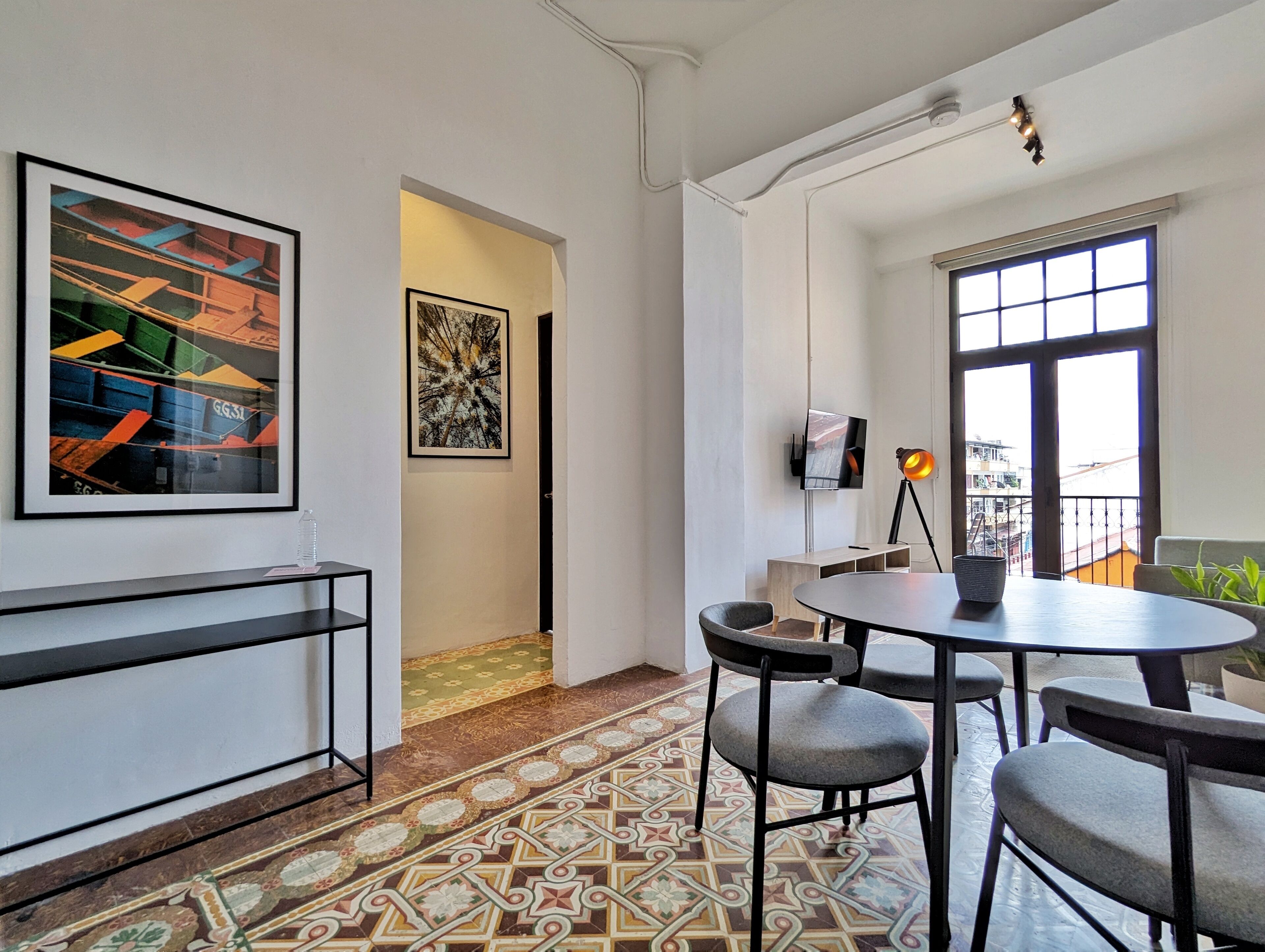 A modern room with a round table, chairs, a TV, artwork on the wall, and a balcony with a view.