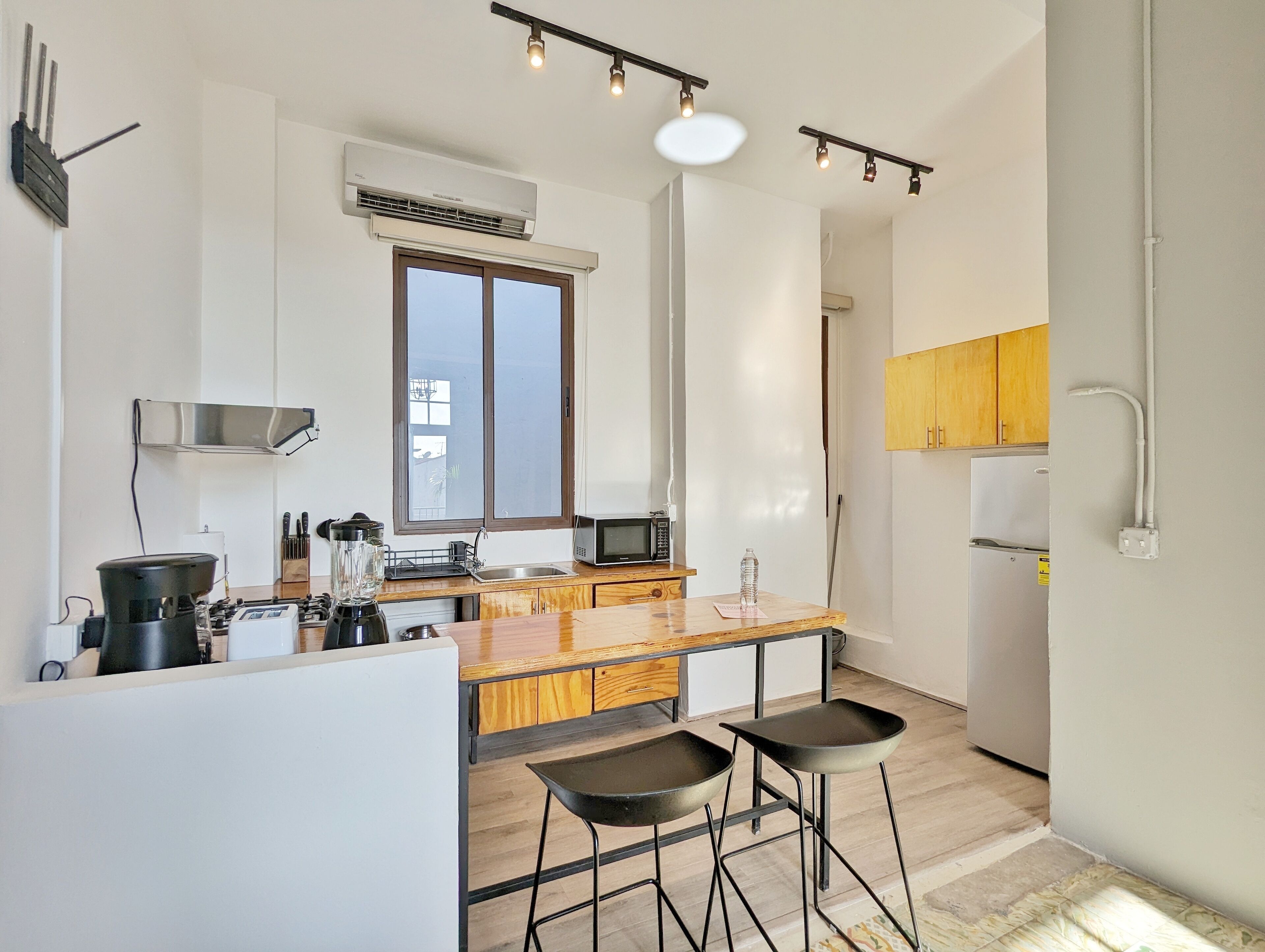 A modern kitchen with a central island, bar stools, a microwave, and an air conditioning unit.