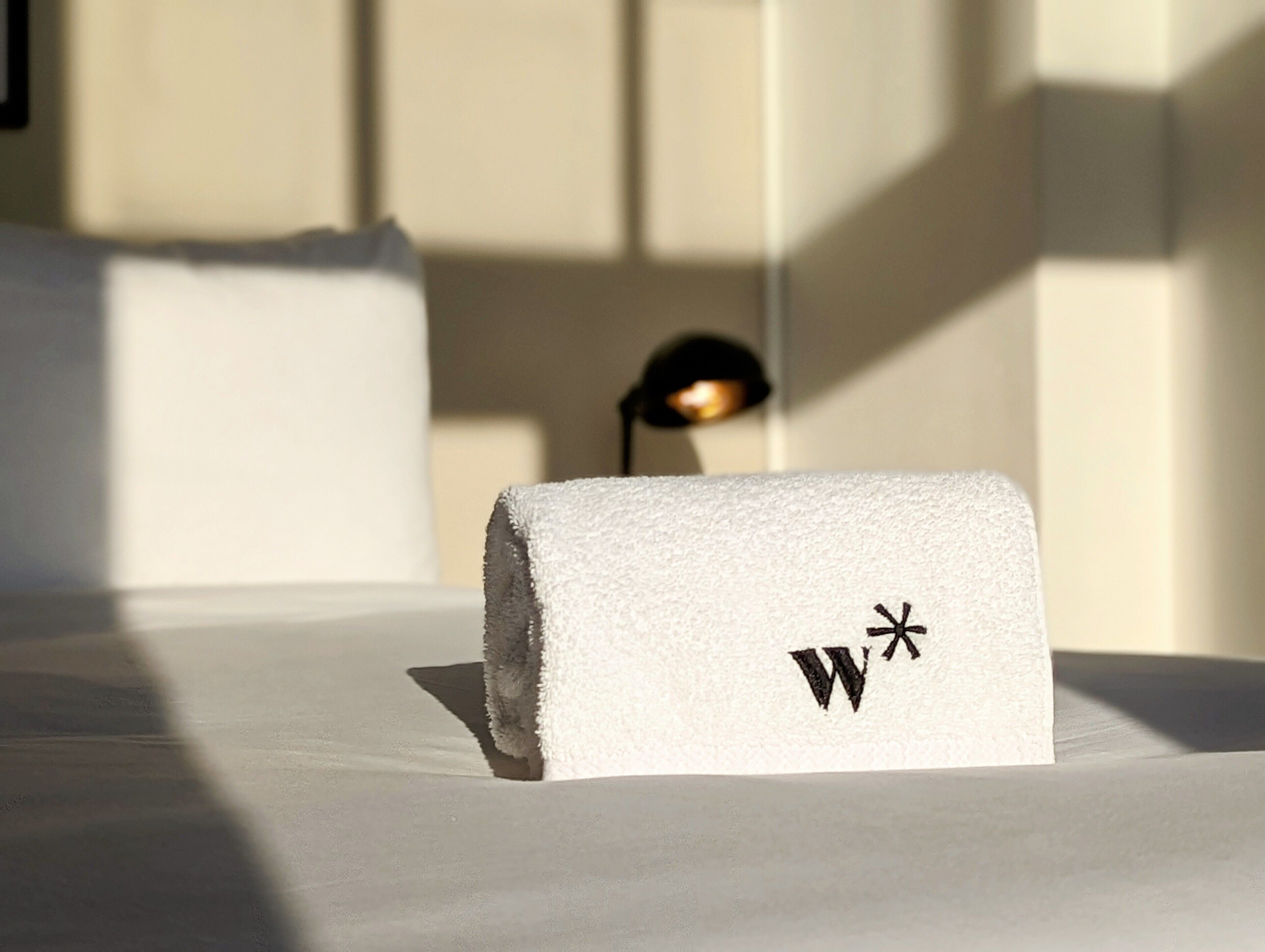 A neatly folded white towel with a logo on a bed in a hotel room.