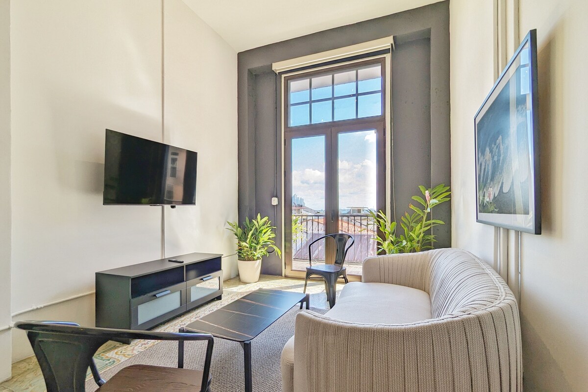 A modern living room with a flat-screen TV, a sofa, a dining table, and two potted plants.