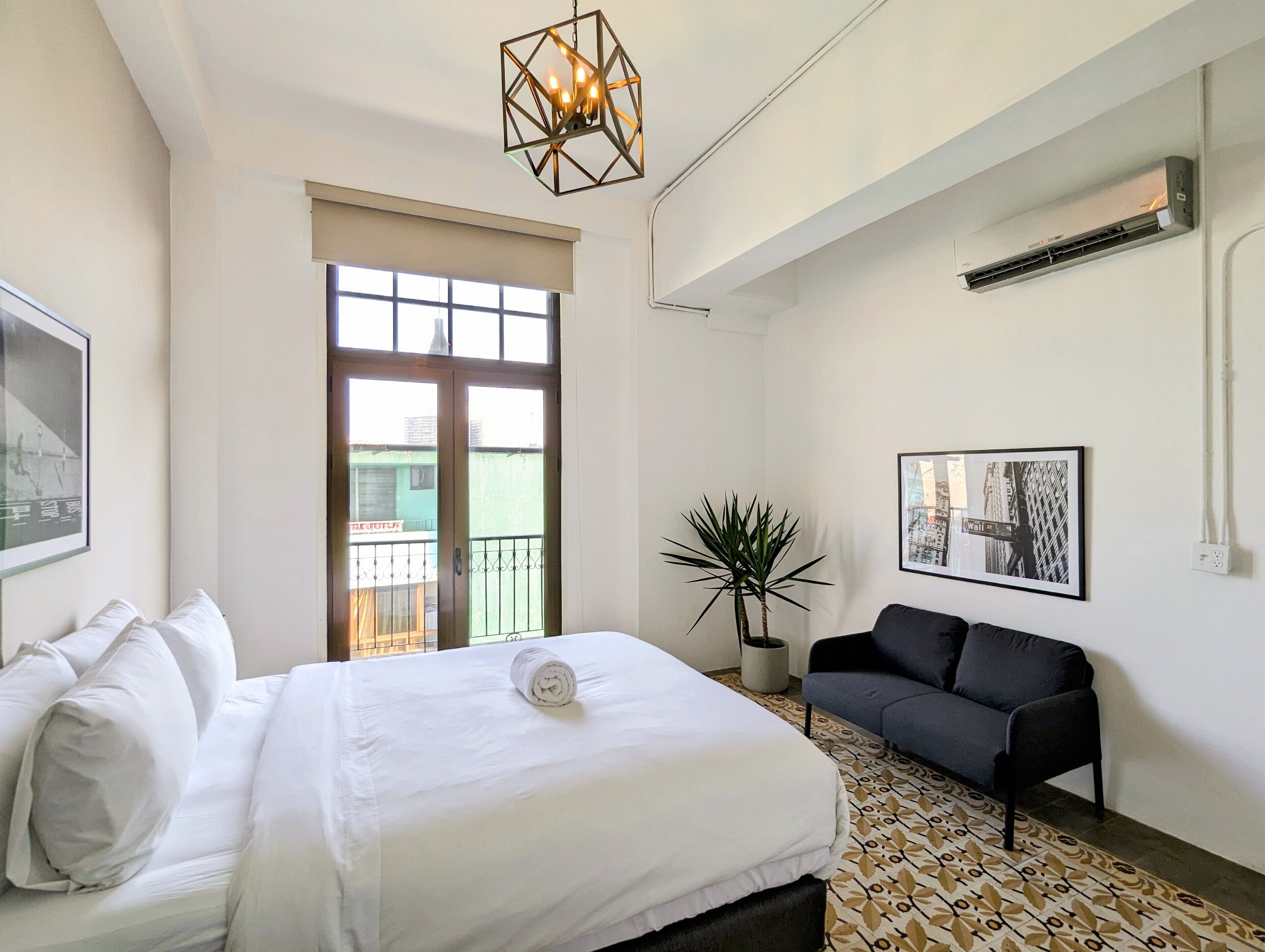 Een hotelkamer met een bed, een bank, een kamerplant en een stadsgezicht op de muur.