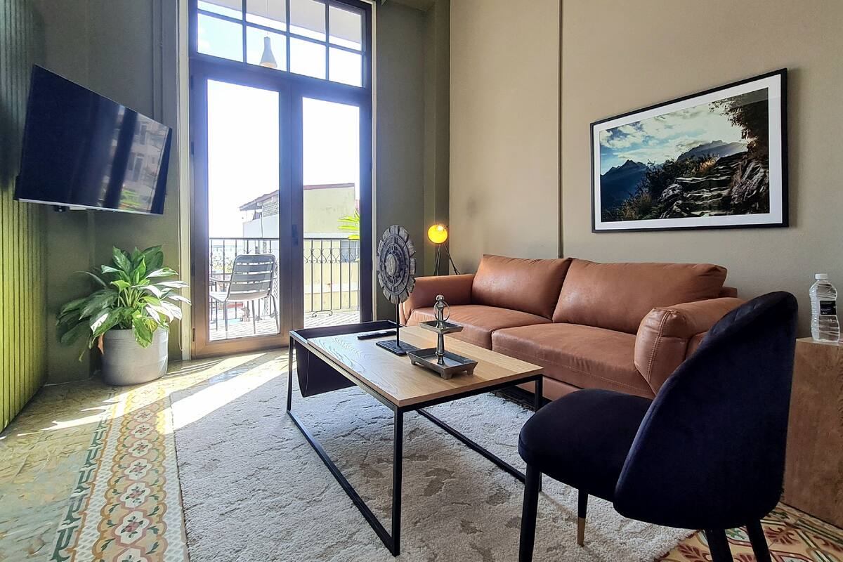 Uma sala de estar com sofá, mesa de centro, televisão na parede, planta em vaso e quadro pendurado na parede.