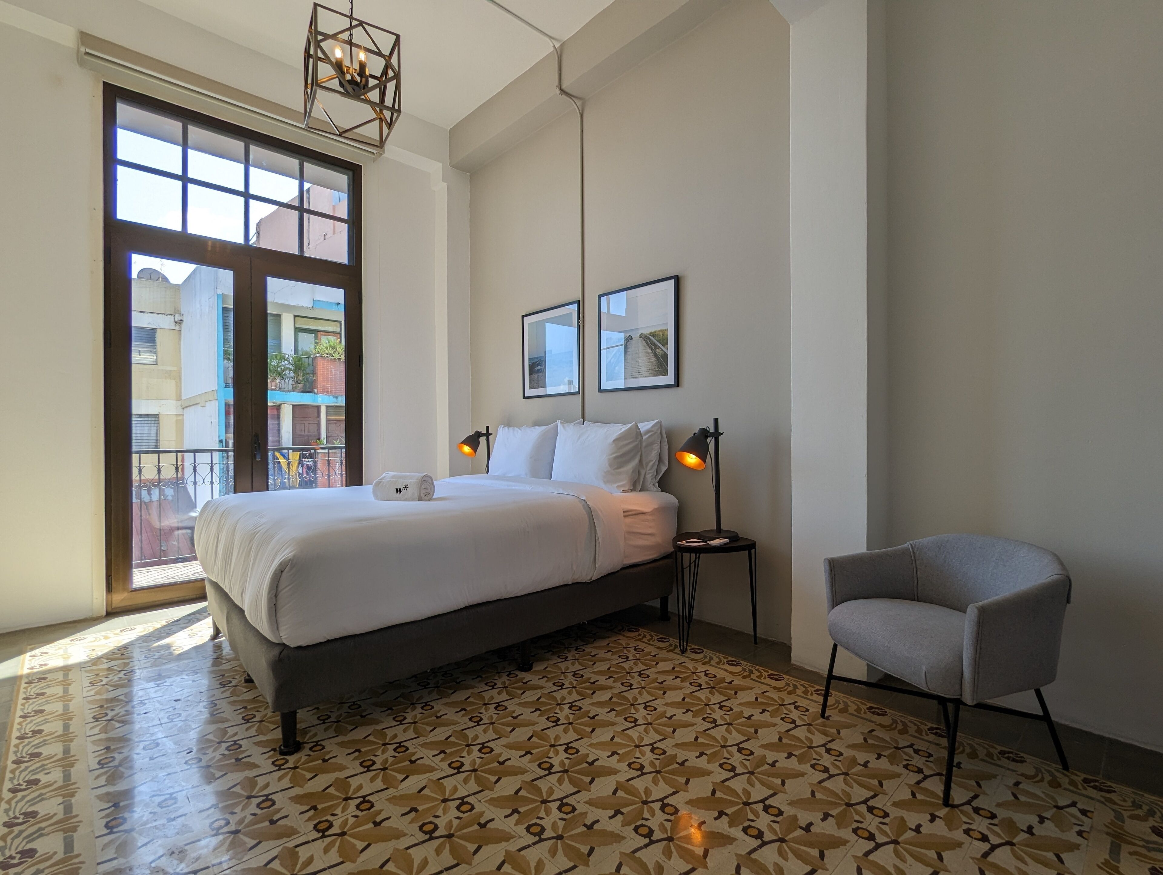 A bedroom with a large bed, two bedside lamps, a chair, and a view of the outside balcony.