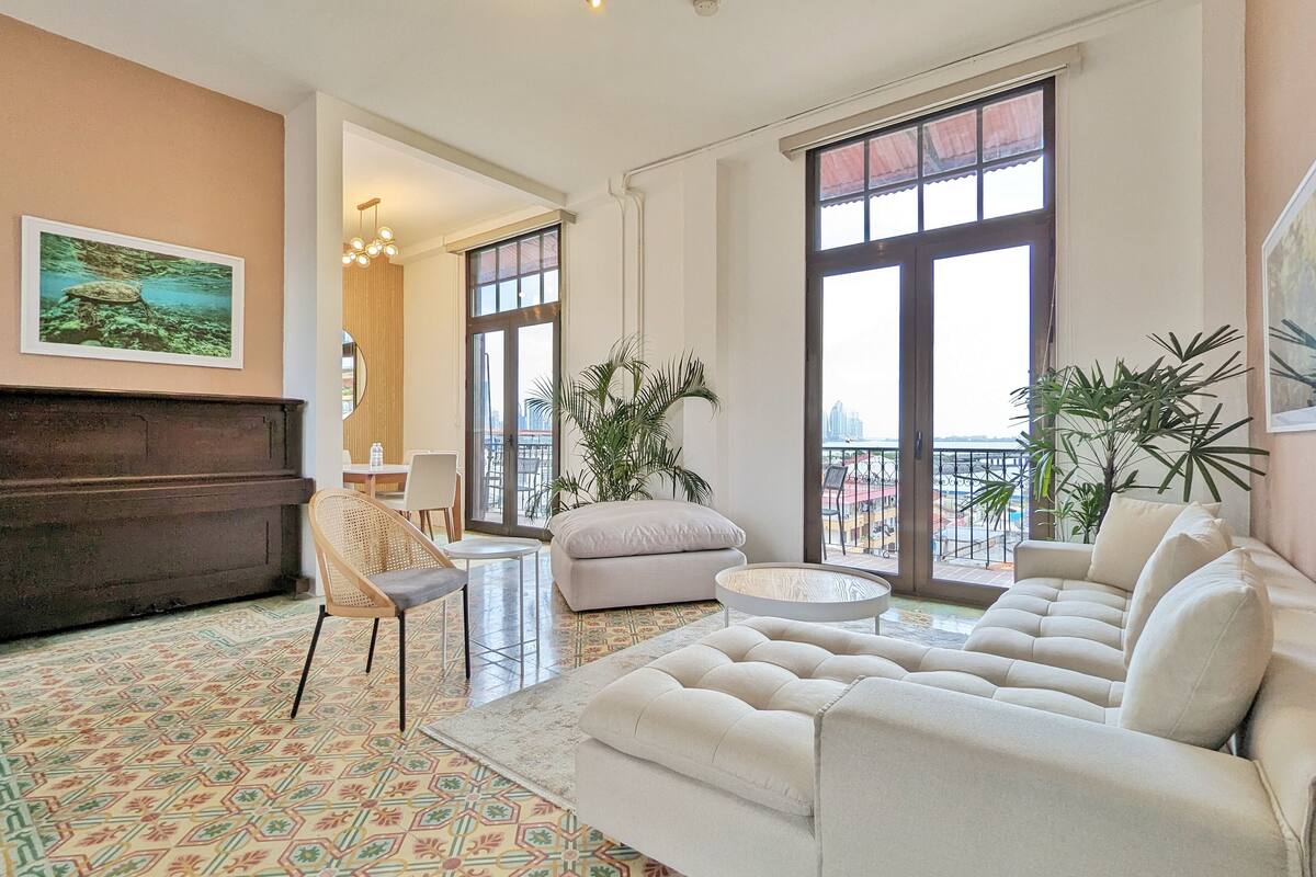 Uma sala de estar ampla com um conjunto de sofás, um espaço de jantar e um piano.