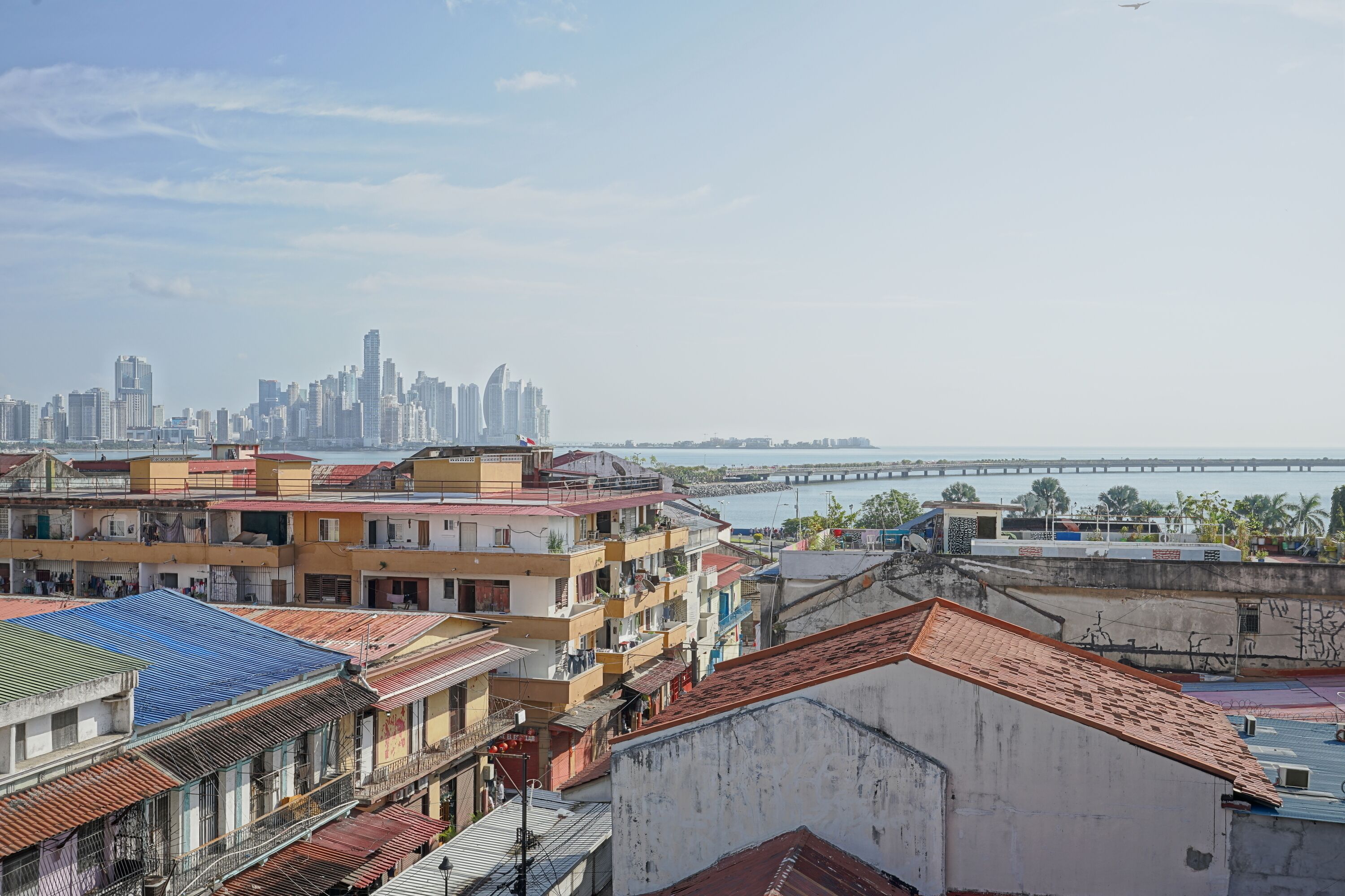 Un paisaje urbano con un puente destacado en la distancia, una mezcla de edificios residenciales y una vista despejada del frente marítimo.