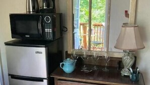 Angolo cottura con forno a microonde, macchina del caffè e bollitore, un frigorifero, un comò in legno con cassetti, uno specchio e una lampada.