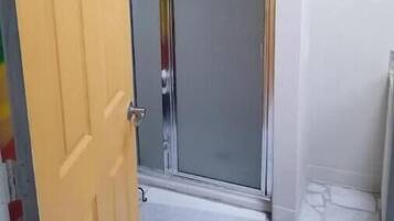 Una habitación con la puerta cerrada, una ducha con puerta de cristal y un espejo en la pared.