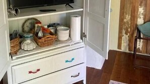 Un mobile bianco con una televisione sopra, scaffali con oggetti da cucina e una porta su un muro rustico.