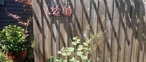 Une porte en bois portant le numéro de maison 22741, entourée de plantes en pot et d’un jardin.