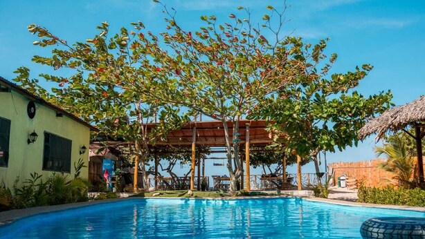 A swimming pool with a wooden deck and a thatched roof structure. - Waikiki Beach Hostel (Dibulla)
