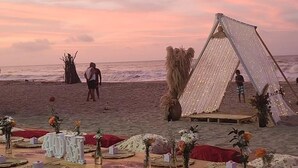 A beach wedding setup with a tent, tables with floral centerpieces, and guests. - Waikiki Beach Hostel (Dibulla)