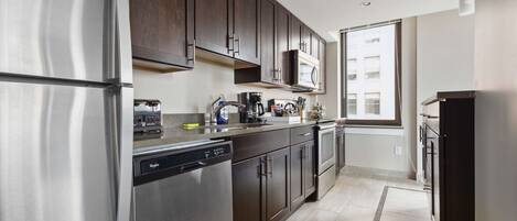 A modern kitchen with stainless steel appliances, dark wooden cabinets, and a window providing natural light.