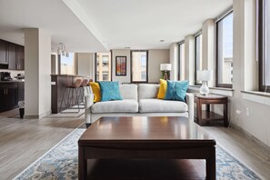 A modern living room with a sofa, coffee table, and a view of the city through large windows. - Modern Downtown Apartment (Detroit)
