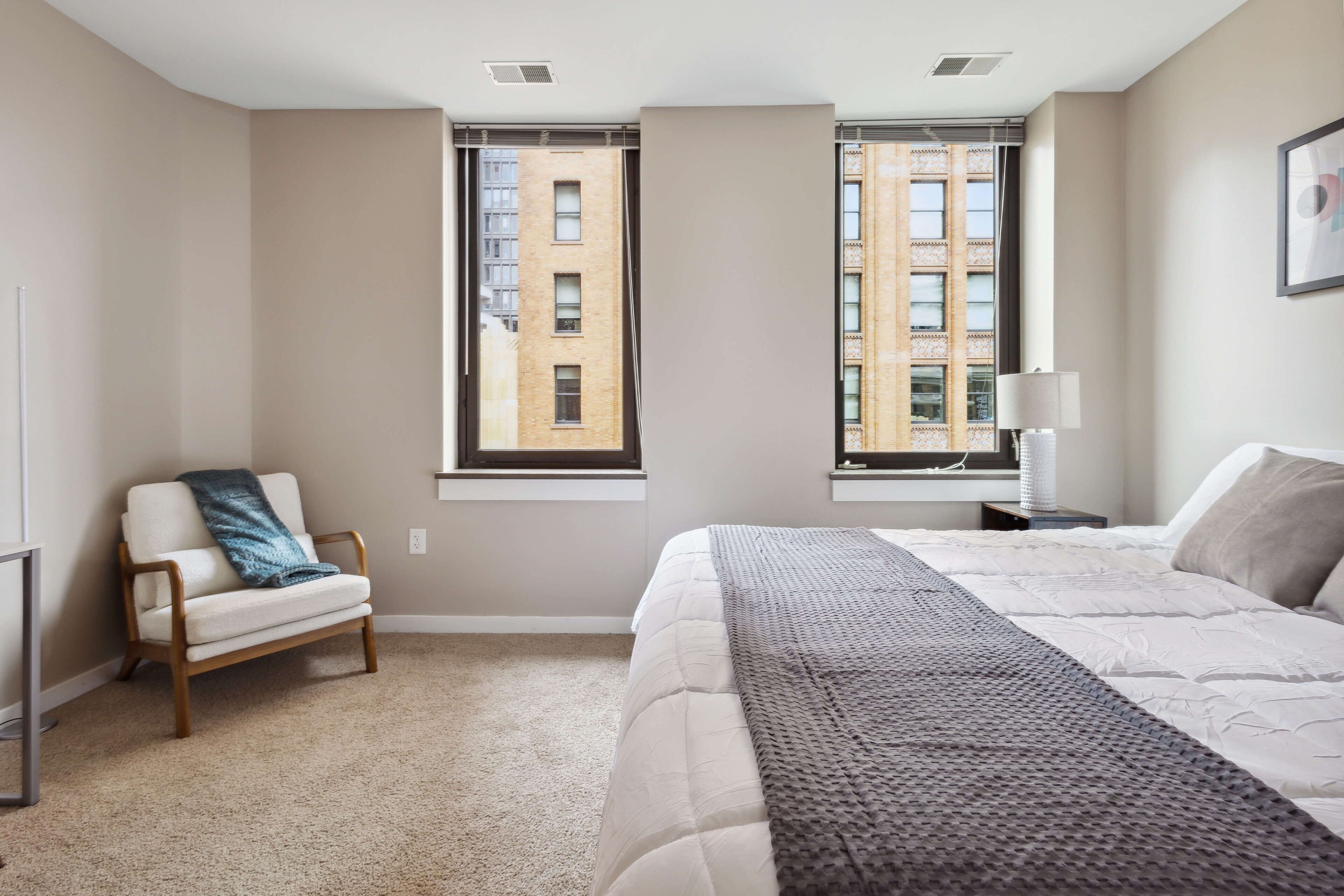 Un dormitorio con una cama, una silla, una ventana y una lámpara.