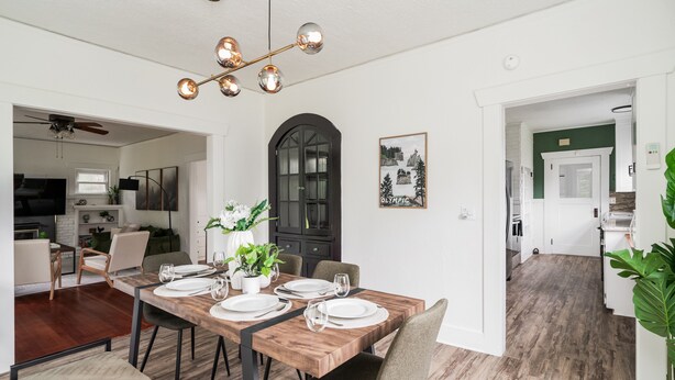 Un coin repas avec une table en bois dressée pour quatre personnes, un lustre et une porte cintrée de couleur noire.
