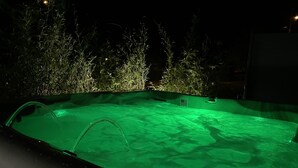 A swimming pool at night with green lighting, surrounded by plants and a dark background. - Gîte des 5 Cépages Avec Jacuzzi (L'Étoile)