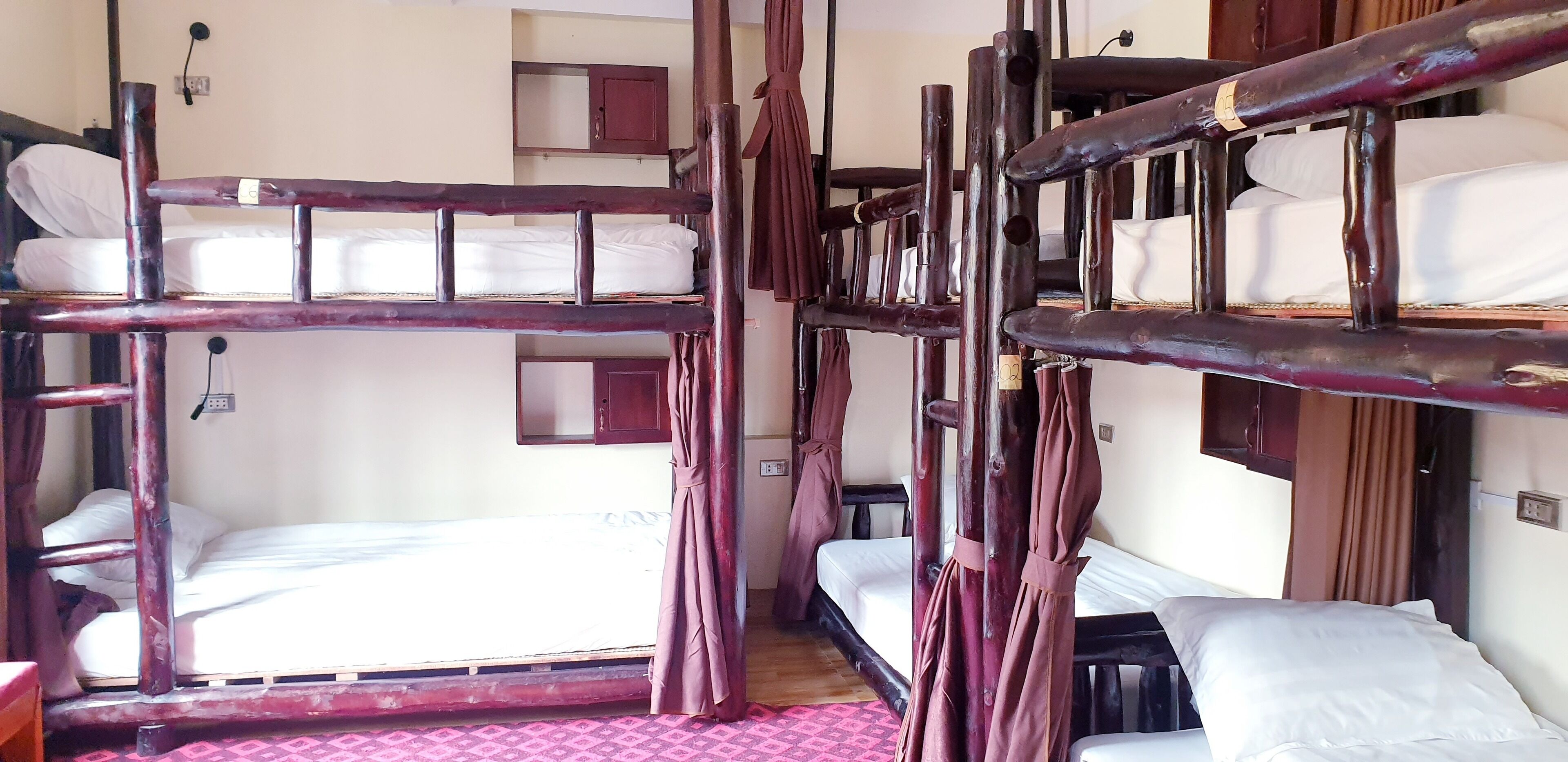 A dormitory room with bunk beds, a small cabinet, and a curtain.