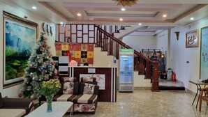 Un vestíbulo de hotel con un árbol de Navidad, una recepción, una escalera e información de servicios en una pared.
