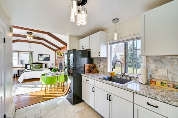 A modern kitchen with white cabinets, a black refrigerator, and a granite countertop.