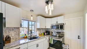 Una cocina moderna con armarios blancos, encimera de granito, electrodomésticos de acero inoxidable y un ventanal con vistas al exterior.