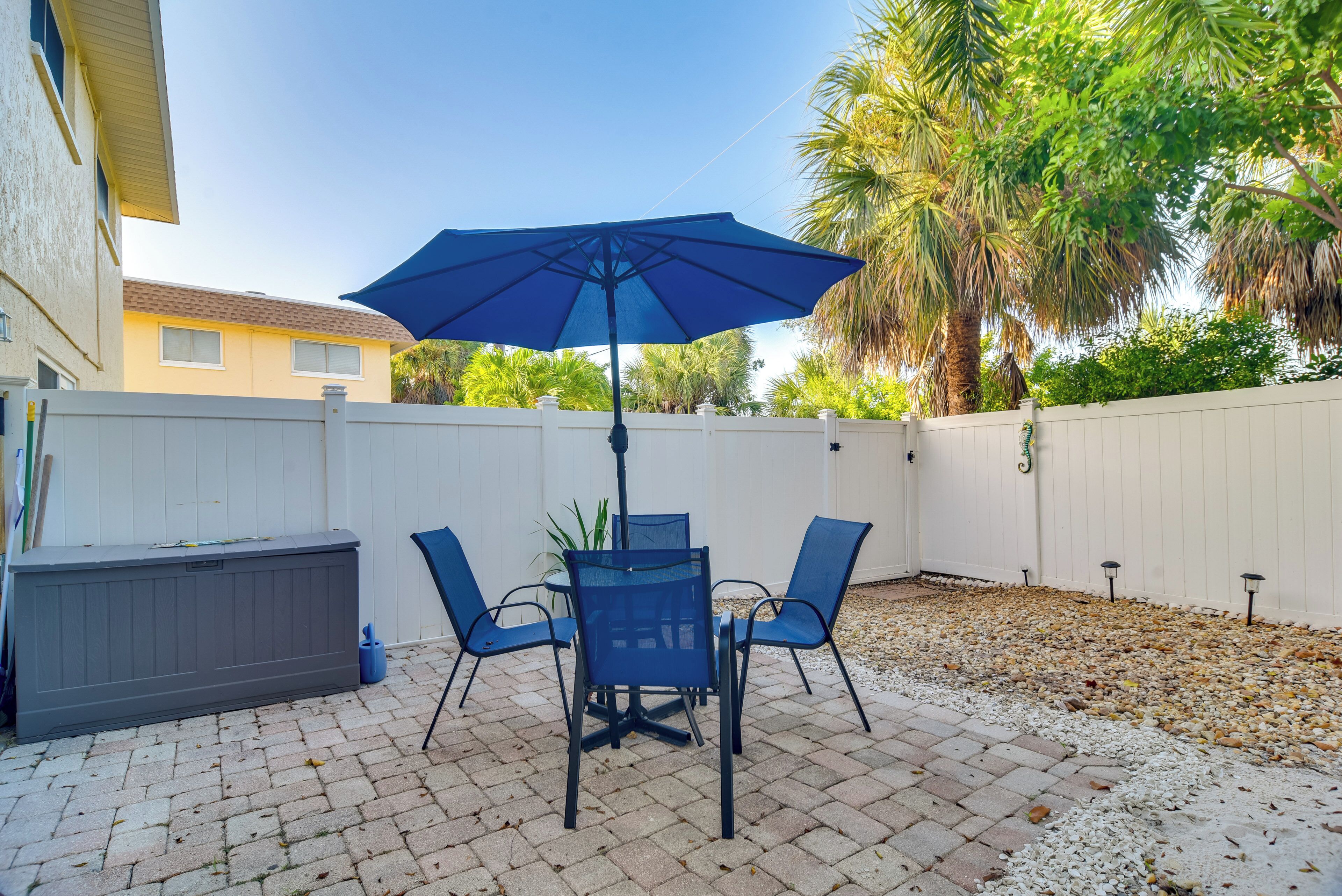 A patio with a table and chairs, a blue umbrella, and a white fence.