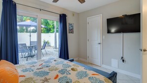 Ein Schlafzimmer mit Bett, Deckenventilator, Fernseher und einer Glastür, die auf eine Terrasse mit Tisch und Stühlen führt.