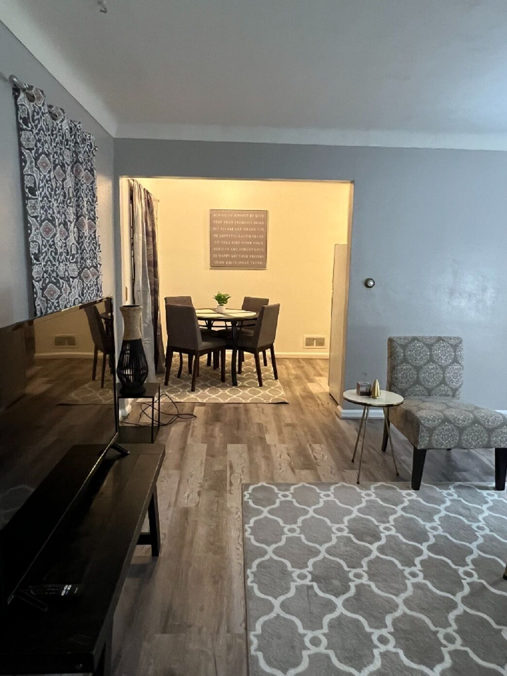 Un salon moderne avec une table basse en bois foncé, un tapis à motifs et un fauteuil à motifs gris.