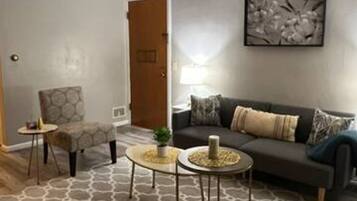 A living room with a grey sofa, two round coffee tables, a patterned rug, and a door in the background.