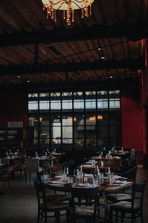 Un restaurante con mesas dispuestas para comer, ventanas amplias y techo de madera.