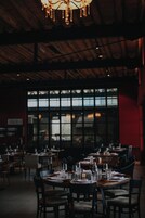 Restaurante com mesas preparadas para refeições, amplas janelas e teto de madeira.