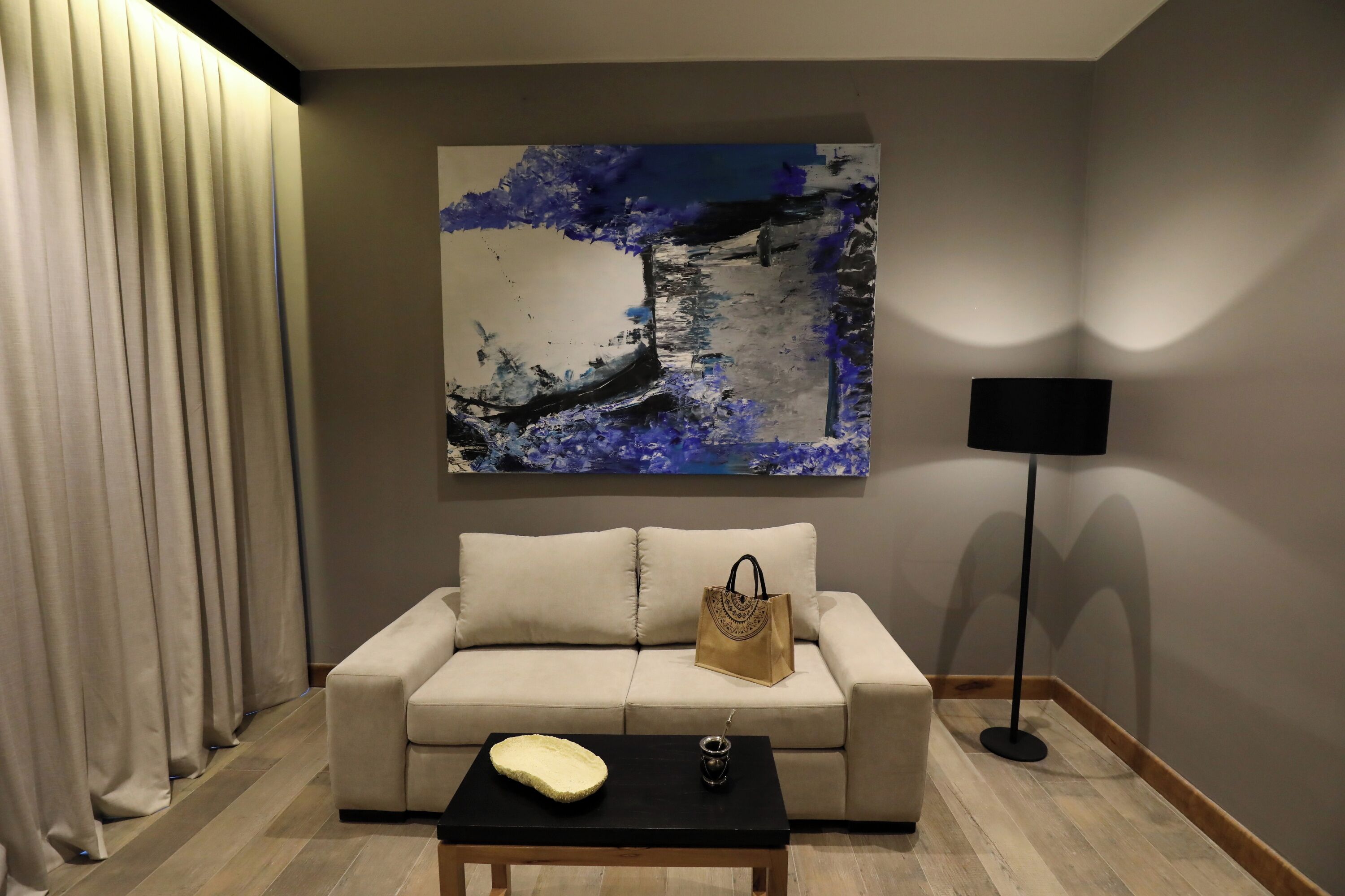 A living room with a beige sofa, a black coffee table, a painting of a tree, and a floor lamp.